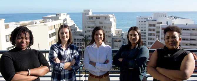 Group of five women standing confidently on a balcony with a city and ocean backdrop, IT Girls at RSAWEB.